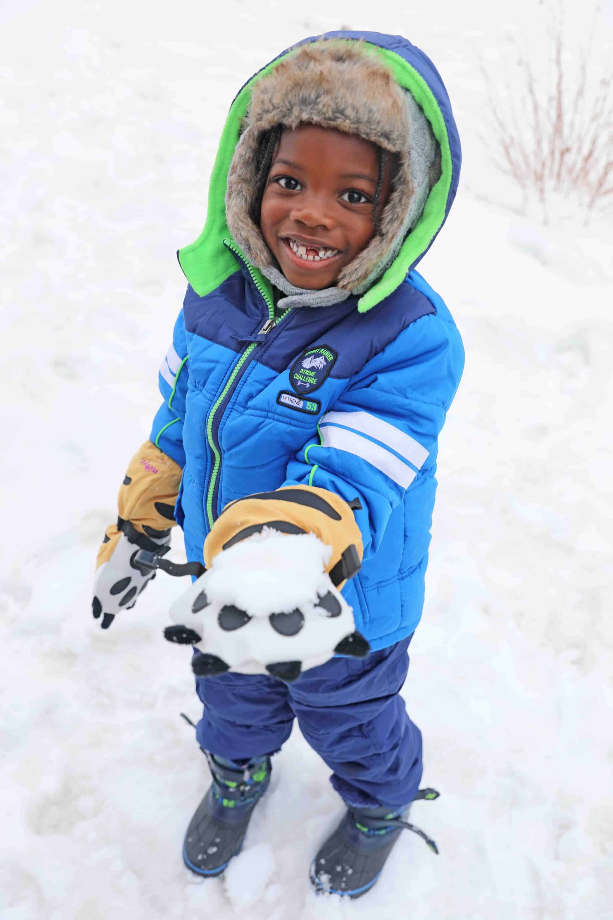 A young boy playing in the snow in his blue snowsuit keeping warm on his families snow trip