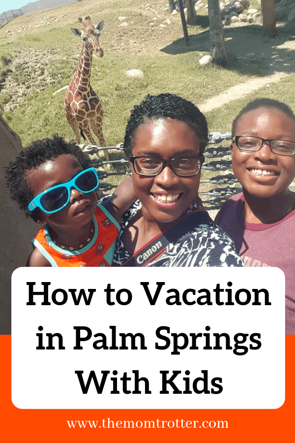 Mom and two kids smiling in front of a giraffe - how to vacation in palm springs with kids