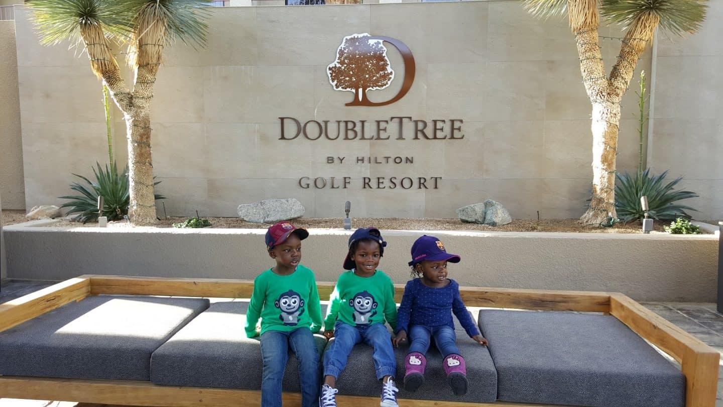 3 kids sitting on a bench in front of the Doubletree by Hilton resort in Palm Springs